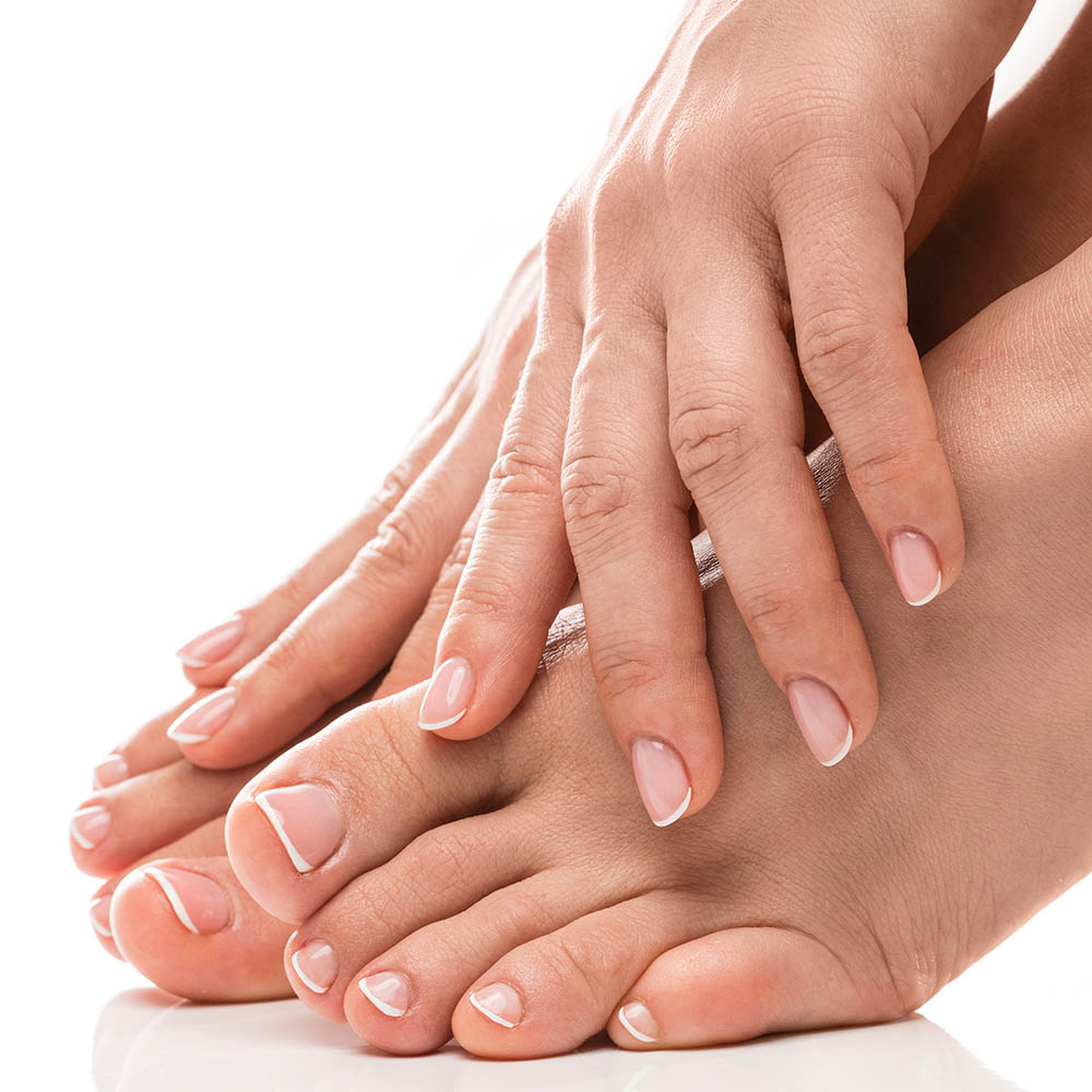 Closeup of female feet and hands with soft skin, french manicure and pedicure on white background